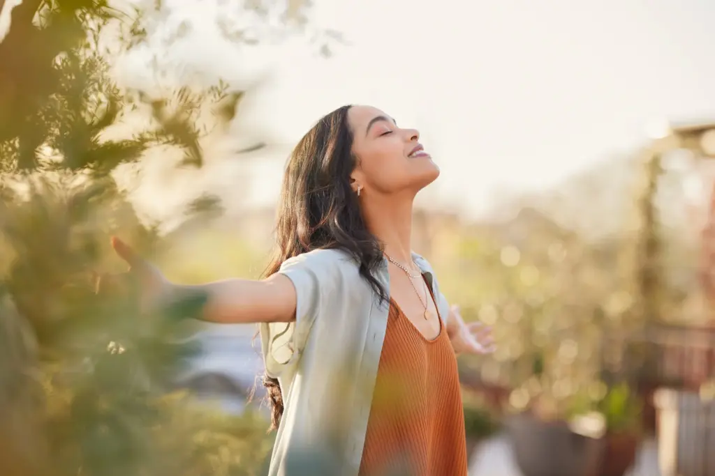 Woman with arms open and eyes closed, enjoying the sunshine outdoors