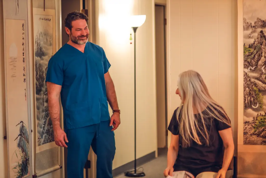Matthew Simone, FNP-BC, in scrubs with a patient in the exam room