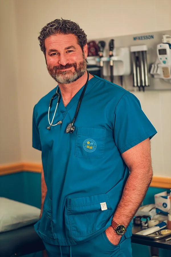 Matthew Simone, FNP-BC, smiling in scrubs in the exam room