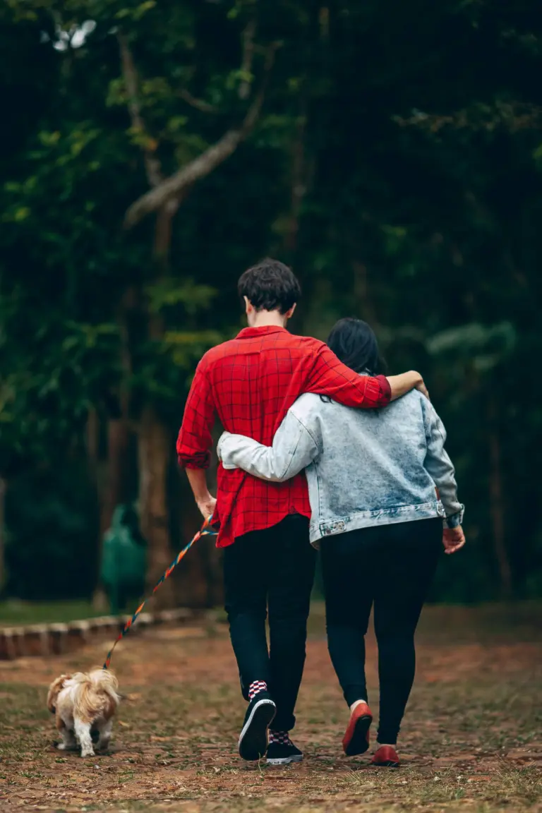 Couple walking arm in arm through the woods with their dog